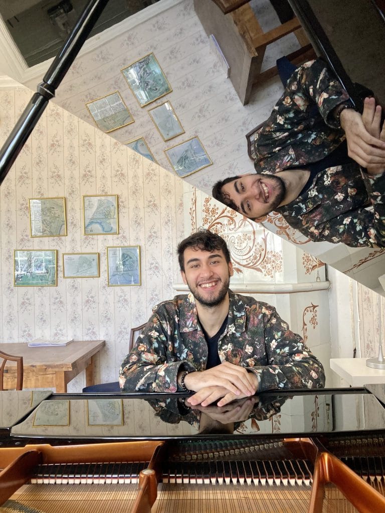 Armaan Madar seated by a grand piano, smiling.