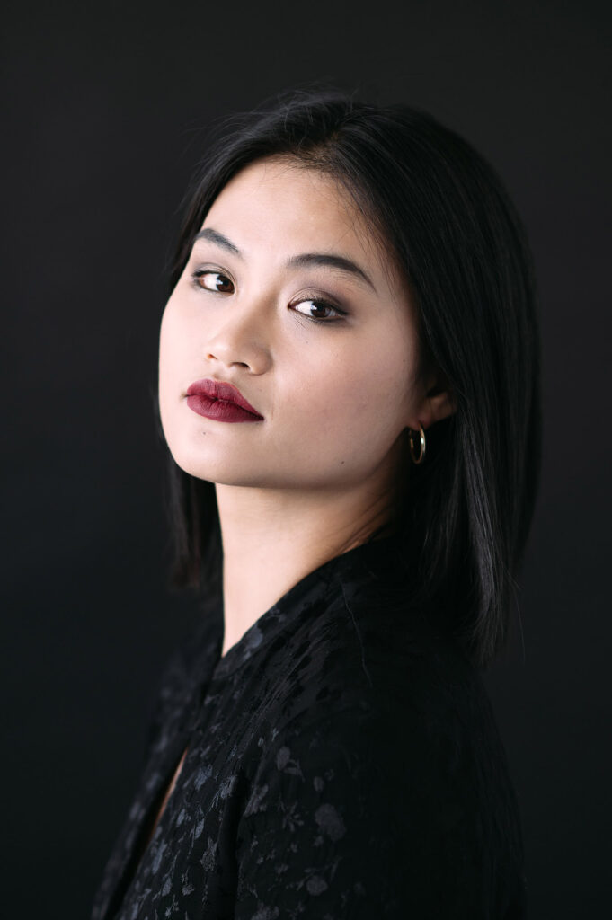 Kasvokuva tummahiuksisesta naisesta mustan taustan edessä